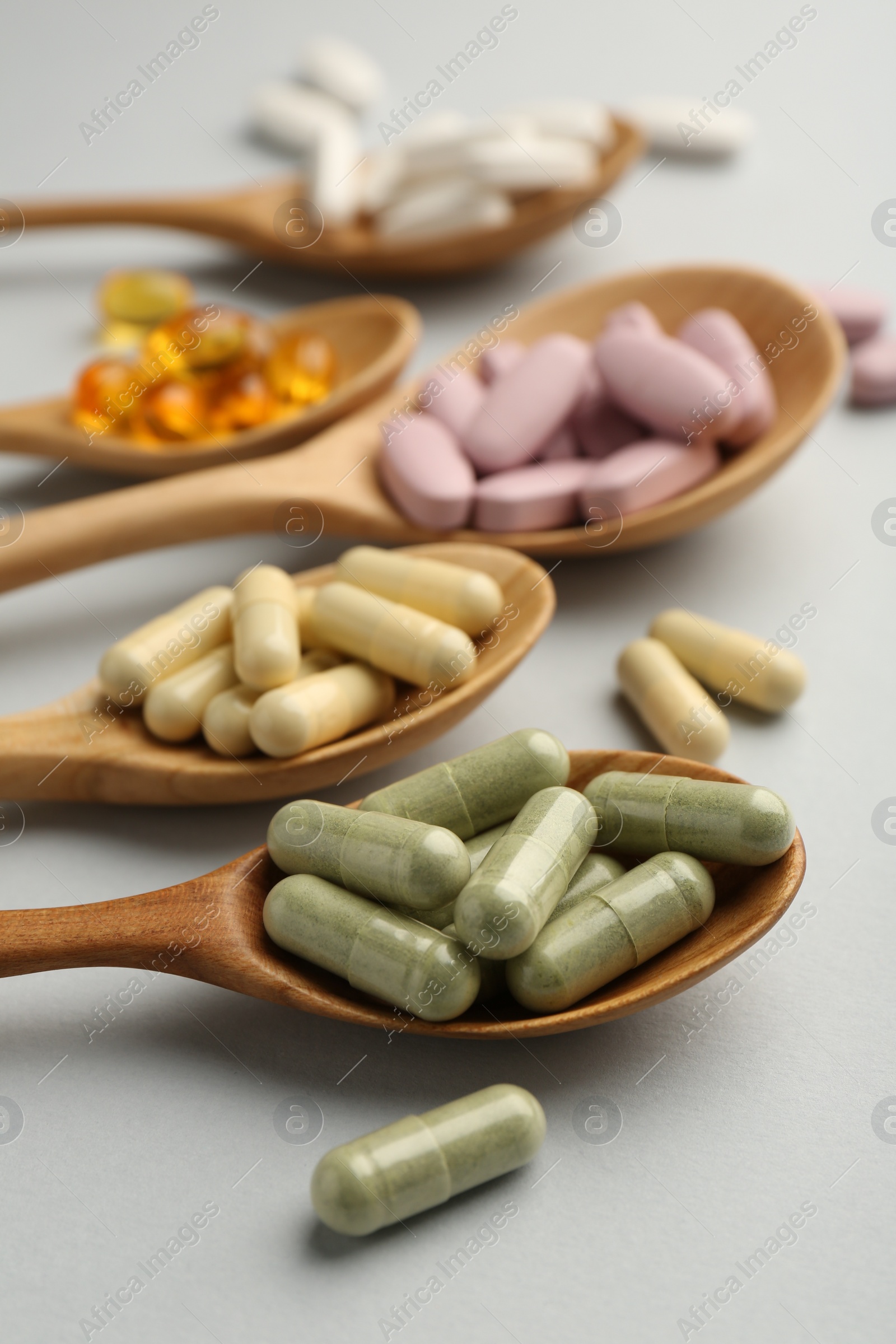 Photo of Different vitamin pills in spoons on light grey background, closeup. Health supplement