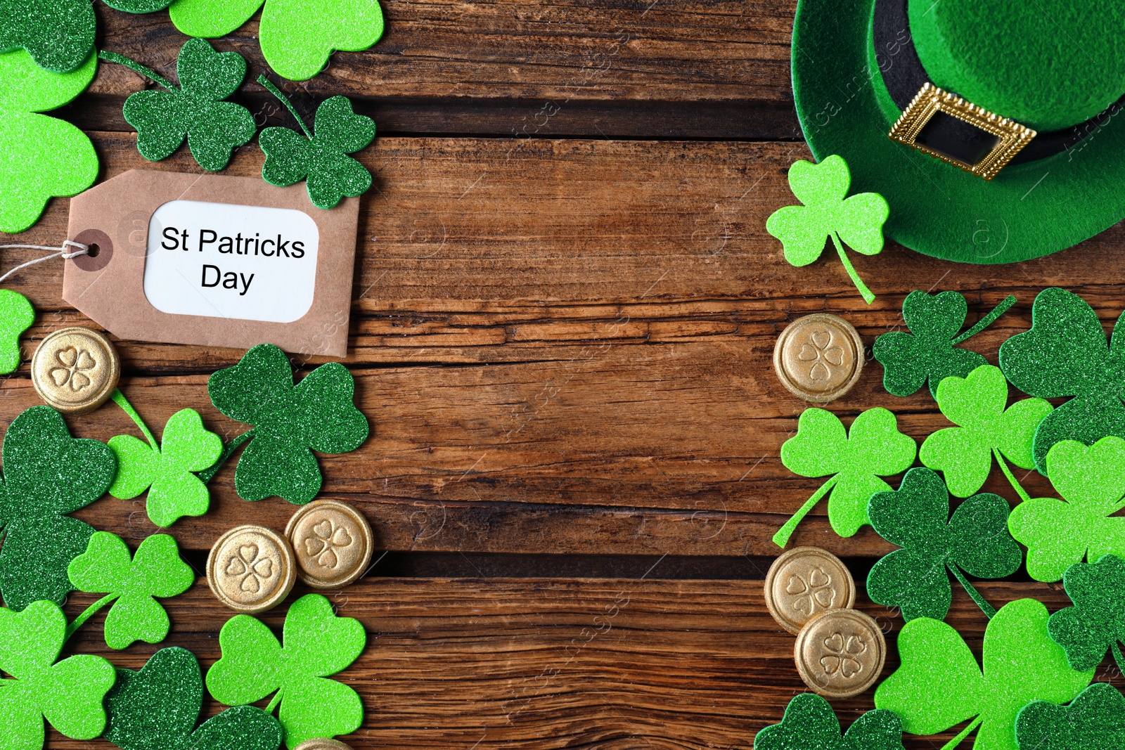 Photo of Frame made of clover leaves and gold coins on wooden table, flat lay with space for text. St. Patrick's Day celebration