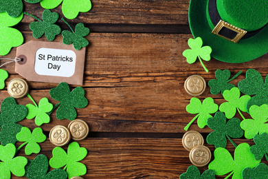 Photo of Frame made of clover leaves and gold coins on wooden table, flat lay with space for text. St. Patrick's Day celebration