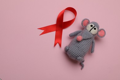 Cute knitted toy mouse and red ribbon on pink background, flat lay with space for text. AIDS disease awareness