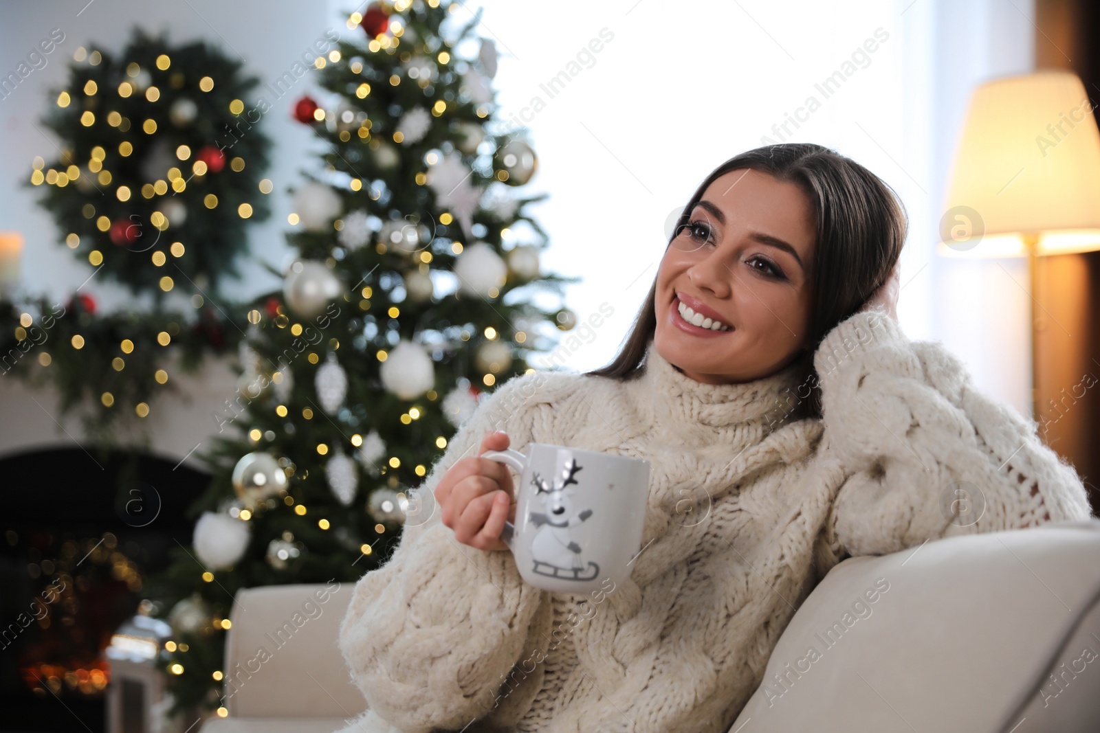 Photo of Beautiful young woman with cup of hot drink in living room decorated for Christmas