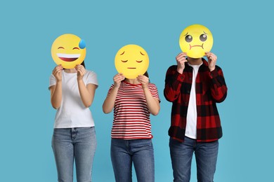 People covering faces with emoticons on light blue background