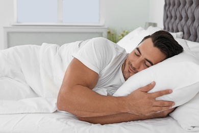 Young man sleeping in bed with soft pillows at home