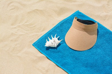 Towel, straw visor cap and seashell on sand, space for text. Beach accessories