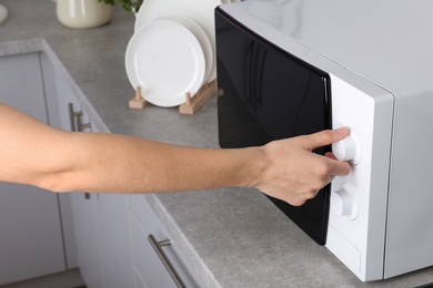 Woman adjusting microwave oven in kitchen, closeup