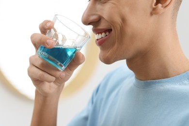 Young man using mouthwash indoors, closeup view