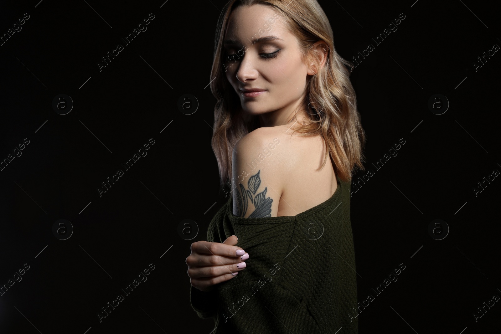 Photo of Beautiful woman with tattoos on arm against black background