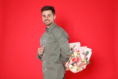 Photo of Young handsome man holding beautiful flower bouquet on red background