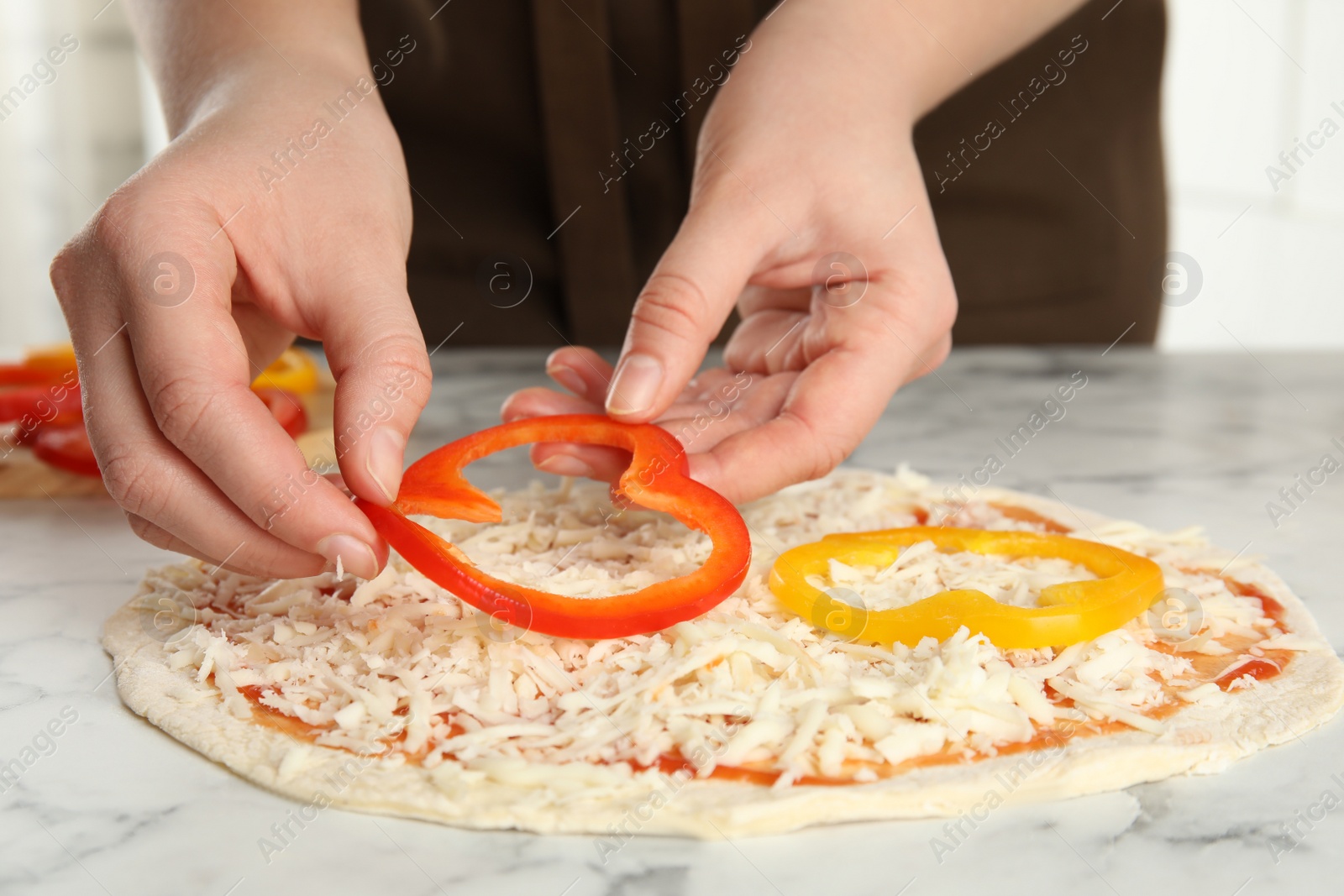 Photo of Woman adding bell pepper to pizza white marble table, closeup