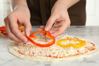 Photo of Woman adding bell pepper to pizza white marble table, closeup