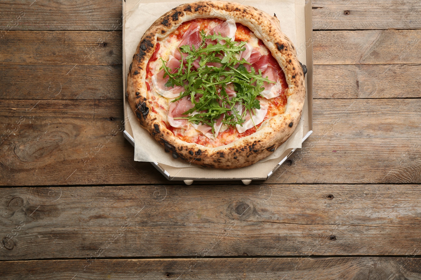 Photo of Tasty pizza with meat and arugula in cardboard box on wooden table, top view