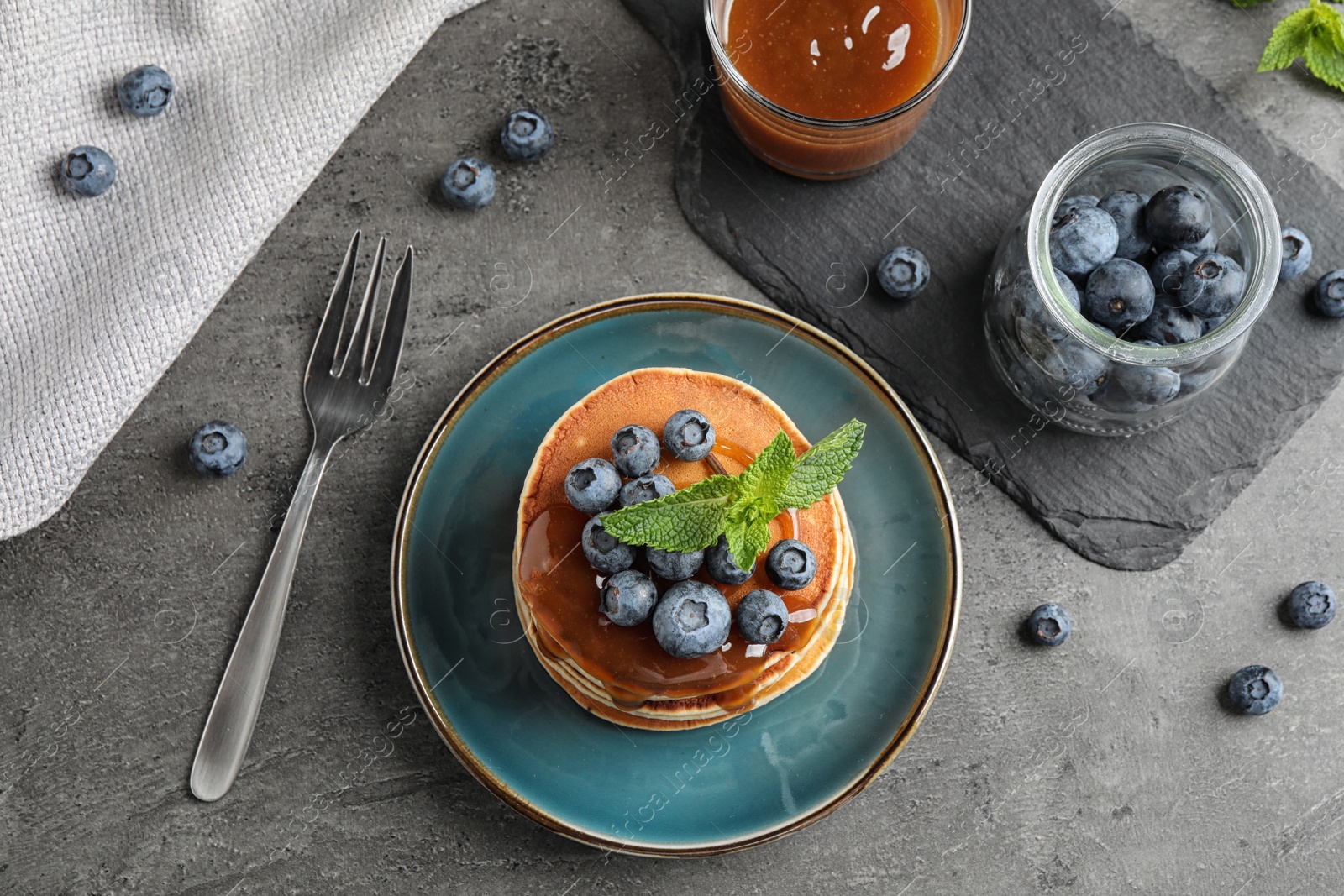 Photo of Tasty pancakes and blueberries served on grey table, flat lay