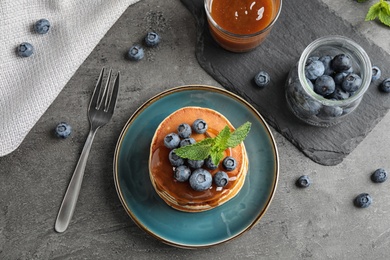 Tasty pancakes and blueberries served on grey table, flat lay