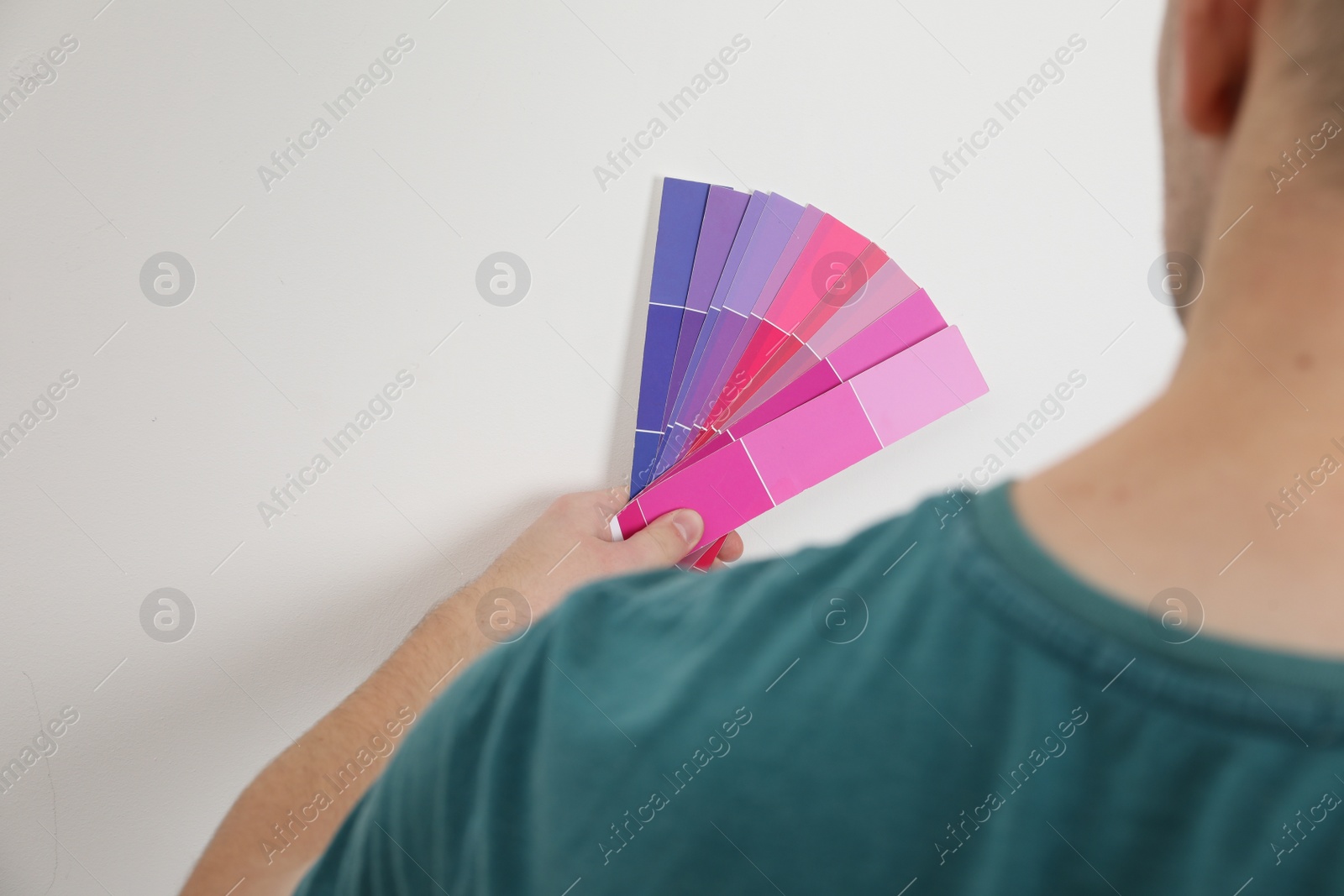 Photo of Man with palette choosing color for painting wall indoors, closeup. Interior design