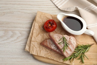 Pieces of delicious tuna with rosemary, tomato and sauce on white wooden table, top view. Space for text