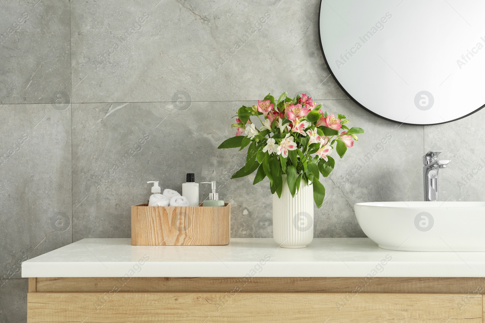 Photo of Vase with beautiful Alstroemeria flowers and toiletries near sink in bathroom