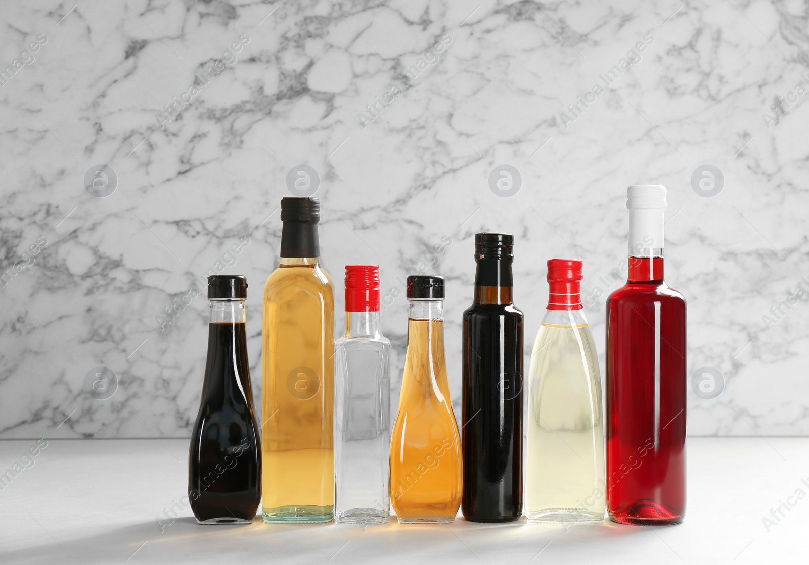 Photo of Bottles with different kinds of vinegar on table against marble background