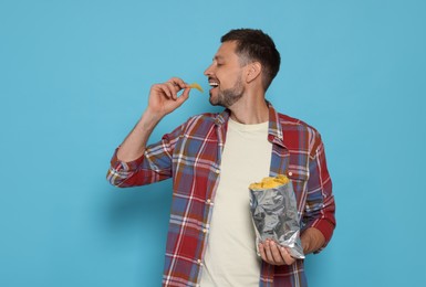 Photo of Handsome man eating potato chips on light blue background