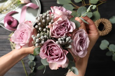 Photo of Florist creating beautiful bouquet at black wooden table, top view