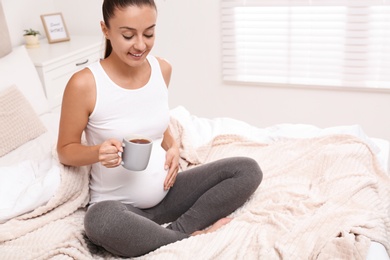 Happy pregnant woman drinking tea at home