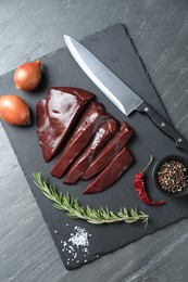 Photo of Cut raw beef liver with rosemary, onions, chili pepper, spices and knife on black table, top view