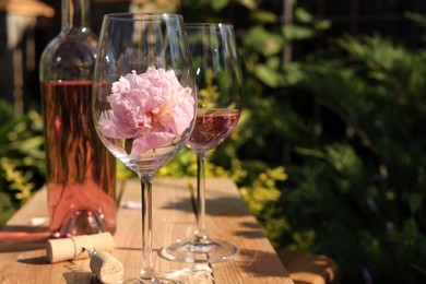 Photo of Bottle and glasses of rose wine near beautiful peonies on wooden table in garden