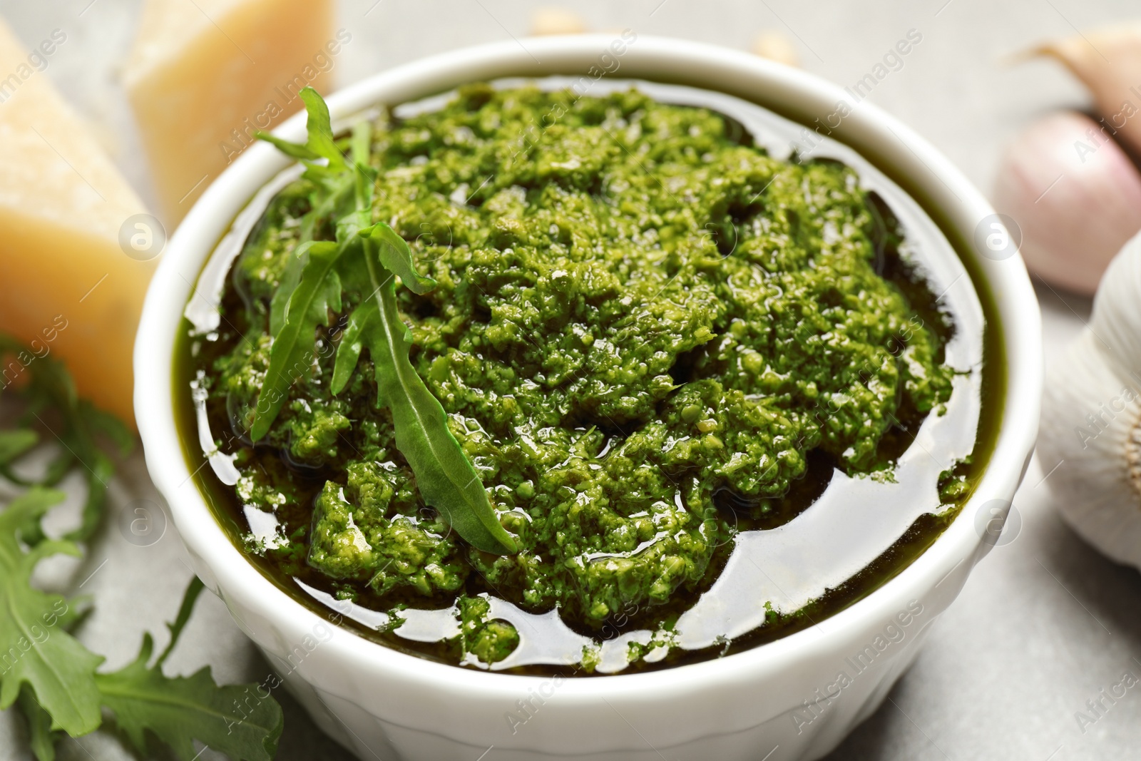 Photo of Bowl of tasty arugula pesto on table, closeup