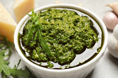 Photo of Bowl of tasty arugula pesto on table, closeup