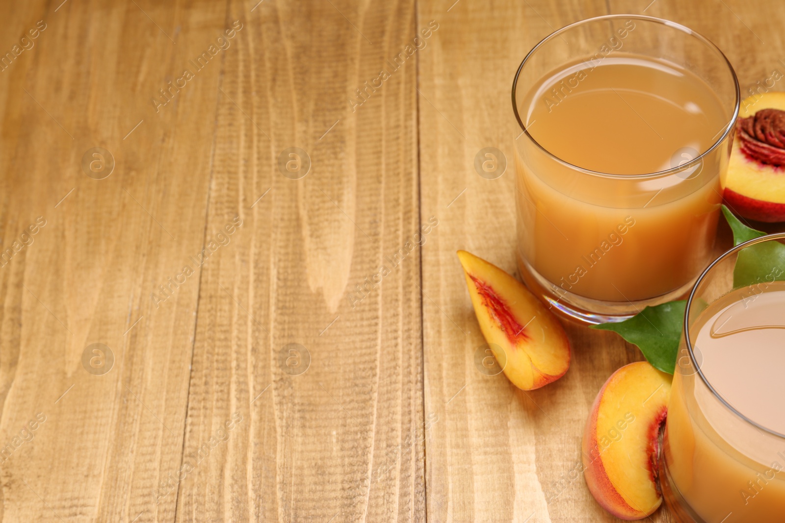 Photo of Glasses of peach juice, fresh fruit and leaves on wooden table. Space for text