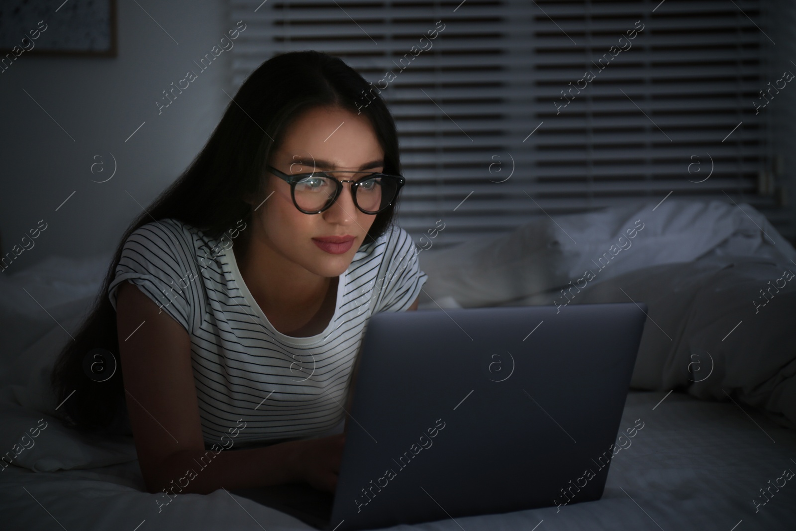 Photo of Young woman using laptop in dark bedroom