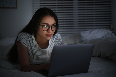 Photo of Young woman using laptop in dark bedroom