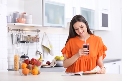 Young woman with glass of tasty healthy smoothie at table in kitchen