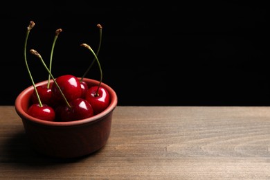 Sweet red cherries in bowl on wooden table, space for text