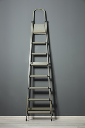 Modern metal step ladder near grey wall