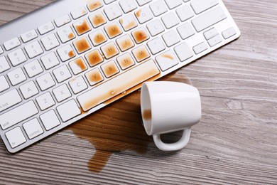 Cup of coffee spilled over computer keyboard on wooden table, flat lay