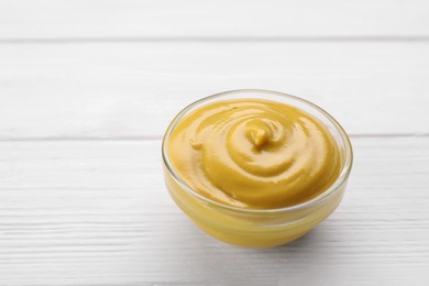 Photo of Bowl with delicious mustard on white wooden table