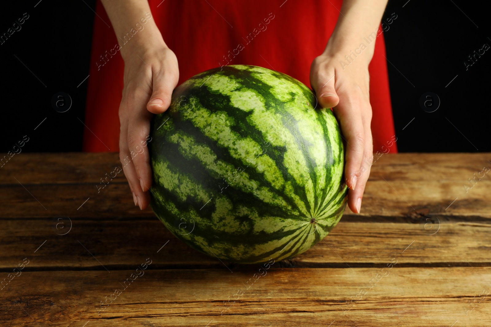 Photo of Woman with delicious ripe watermelon at wooden table against black background, closeup