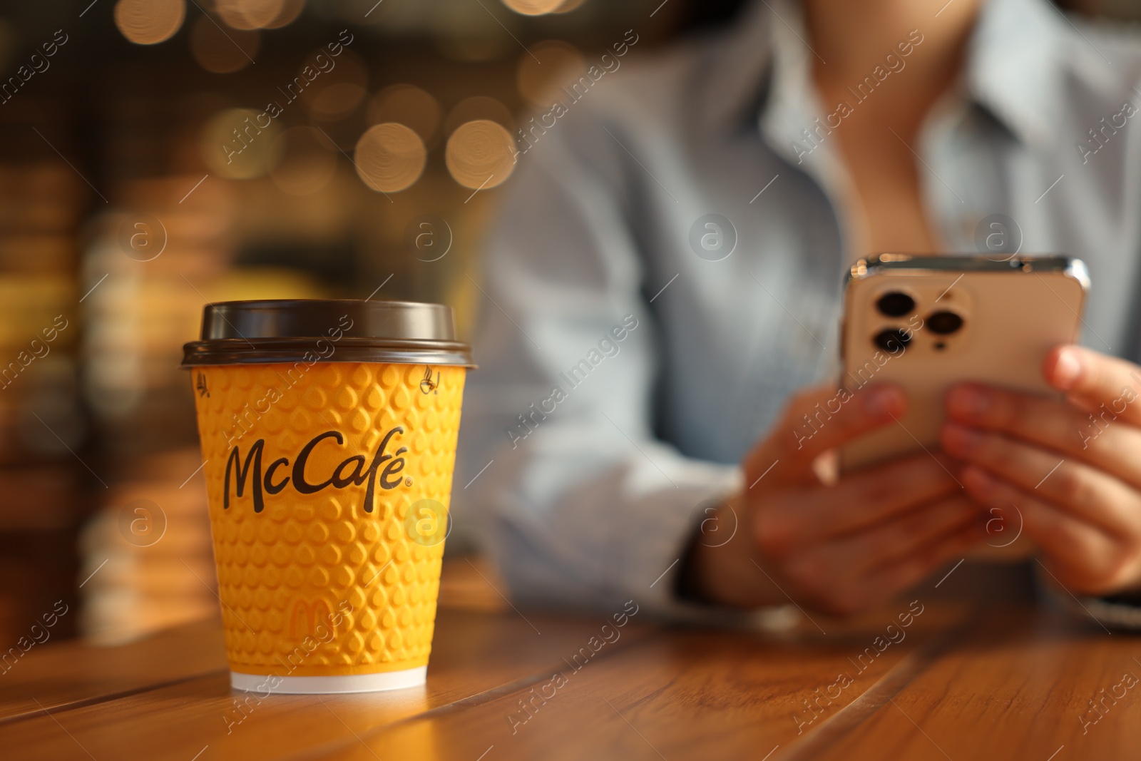 Photo of Lviv, Ukraine - September 26, 2023: Woman with hot McDonald's drink and smartphone at wooden table in cafe, selective focus. Space for text