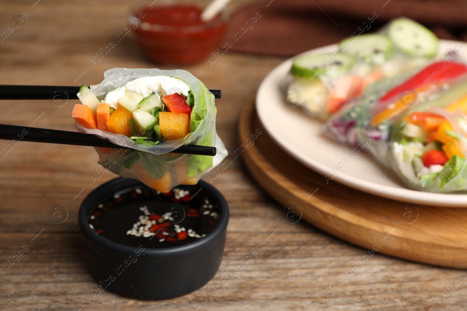 Photo of Delicious roll wrapped in rice paper above soy sauce at wooden table, closeup