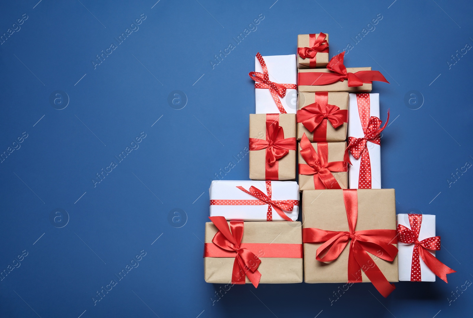 Photo of Christmas tree shape of gift boxes on blue background, flat lay. Space for text