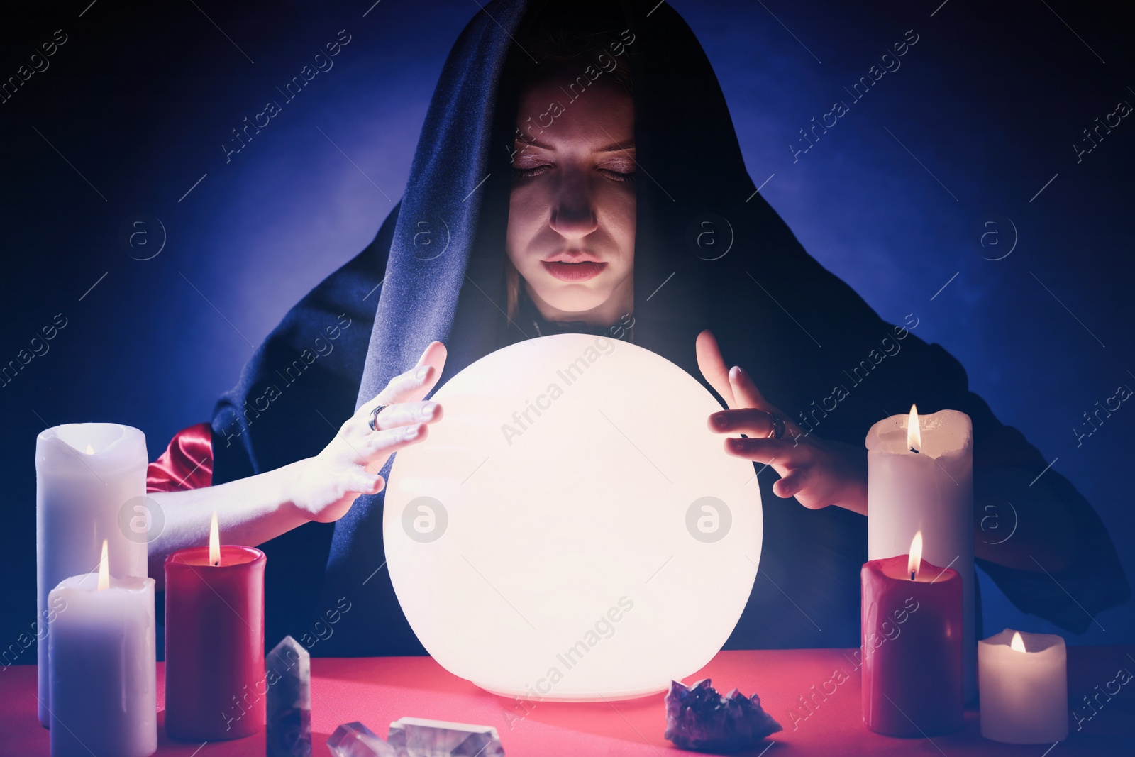 Photo of Soothsayer using glowing crystal ball to predict future at table in darkness. Fortune telling