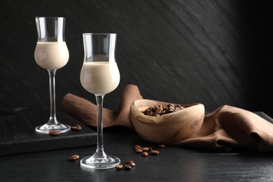 Photo of Coffee cream liqueur in glasses and beans on black wooden table