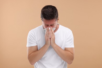 Photo of Allergy symptom. Man sneezing on light brown background
