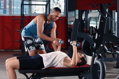 Happy trainer showing woman how to do exercise properly in modern gym