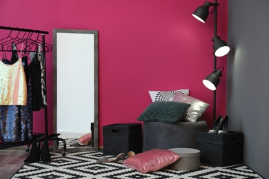 Photo of Dressing room interior with clothes rack, mirror and soft pillows