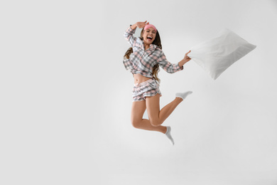 Photo of Beautiful woman with pillow jumping on light grey background. Bedtime