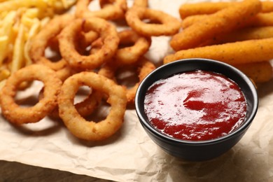 Photo of Bowl with tasty ketchup and snacks on parchment, selective focus. Space for text