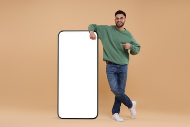 Image of Man pointing at huge mobile phone with empty screen on dark beige background. Mockup for design