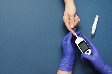 Photo of Diabetes. Doctor checking patient's blood sugar level with glucometer on blue background, top view. Space for text