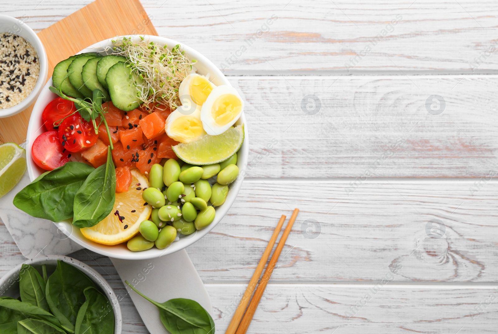 Photo of Delicious poke bowl with quail eggs, fish and edamame beans on white wooden table, flat lay. Space for text